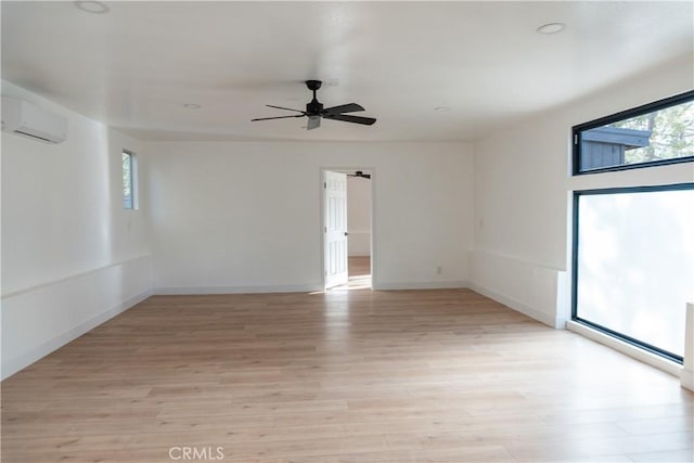 empty room featuring ceiling fan, a wall mounted AC, and light hardwood / wood-style flooring