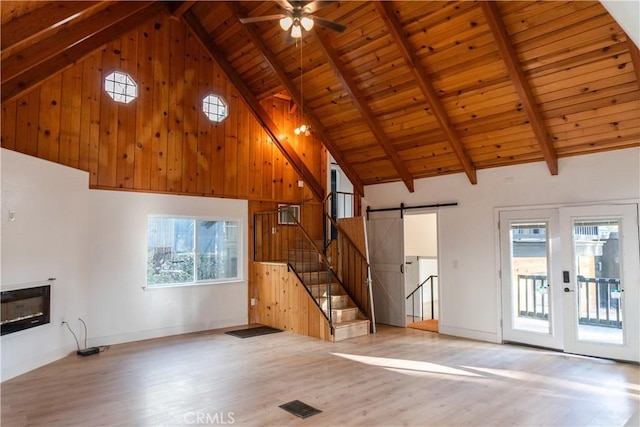 unfurnished living room with a barn door, wood ceiling, beam ceiling, and light hardwood / wood-style flooring