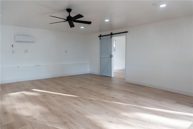 unfurnished room with ceiling fan, a barn door, a wall mounted AC, and light hardwood / wood-style floors