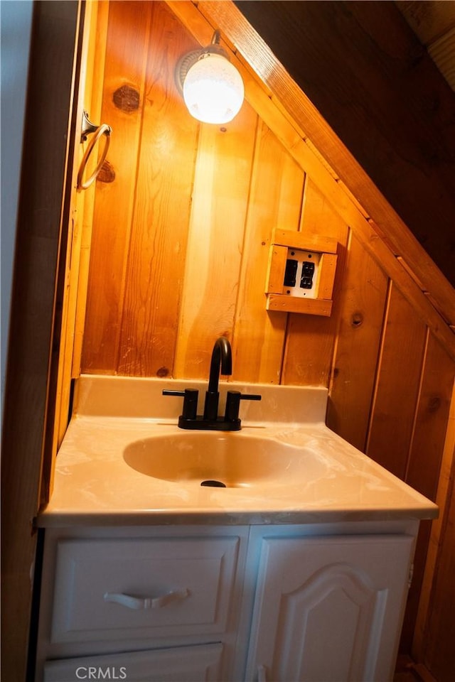 bathroom featuring lofted ceiling, wooden walls, and sink