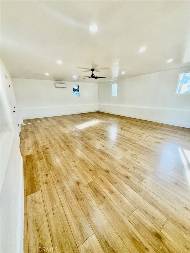 unfurnished room featuring ceiling fan, a wall mounted AC, and light hardwood / wood-style floors