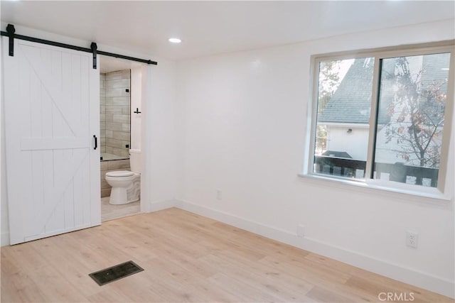 interior space featuring ensuite bath, wood-type flooring, and a barn door