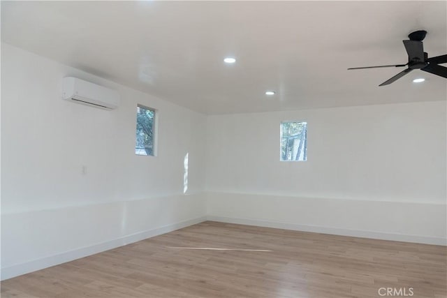 spare room featuring a wall mounted AC, ceiling fan, and light hardwood / wood-style flooring