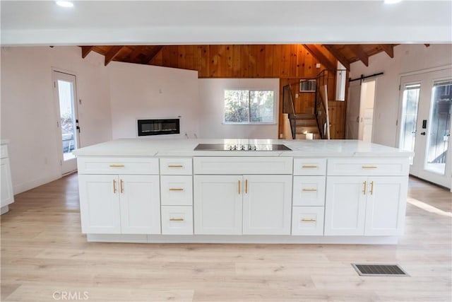 kitchen with lofted ceiling with beams, a barn door, white cabinets, and black electric cooktop