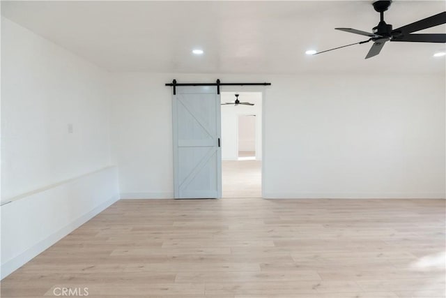 unfurnished room featuring ceiling fan, a barn door, and light wood-type flooring