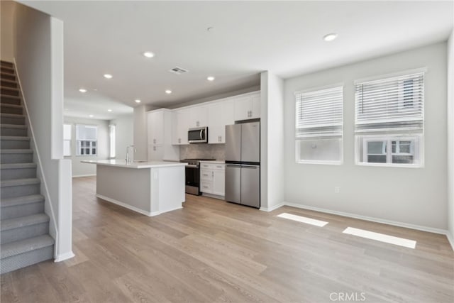 2718 Crozier Ct, Pomona, CA 91767 - kitchen featuring appliances with stainless steel finishes, white cabinetry, a center island with sink, light wood-style flooring, and baseboards