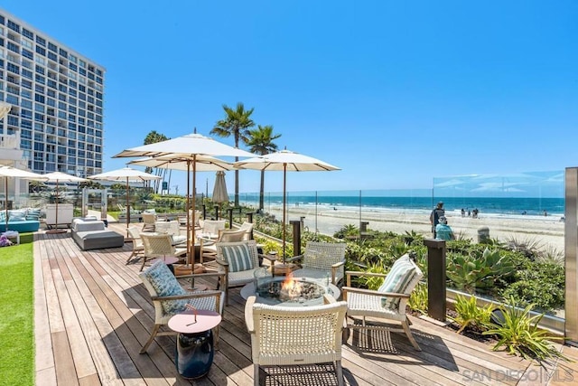 wooden deck featuring a water view, an outdoor fire pit, and a view of the beach