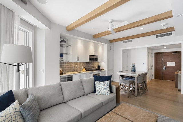 living room featuring sink, light wood-type flooring, beverage cooler, ceiling fan, and beam ceiling