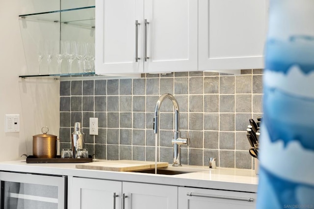 bar with tasteful backsplash, sink, beverage cooler, and white cabinets