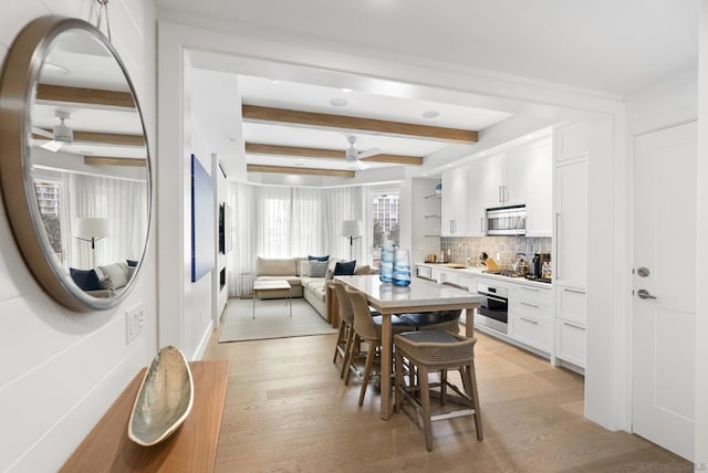 dining space featuring beamed ceiling, ceiling fan, and light wood-type flooring