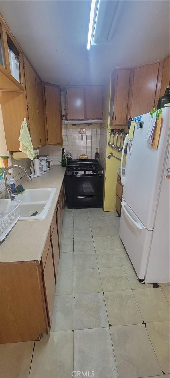 kitchen with sink, light tile patterned floors, white refrigerator, black gas range, and decorative backsplash