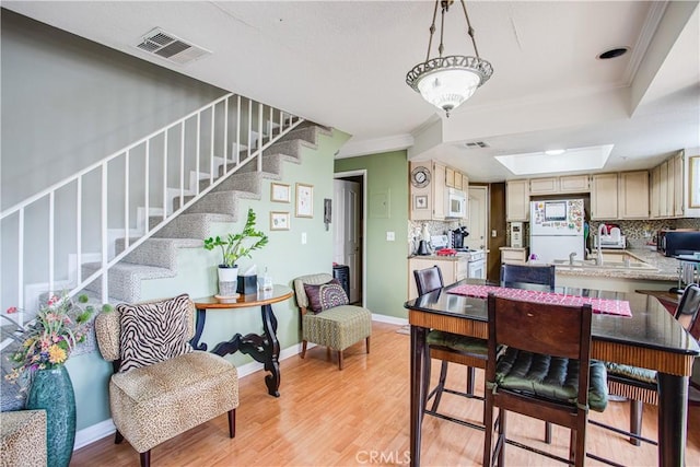 dining space with ornamental molding, sink, light wood-type flooring, and a tray ceiling