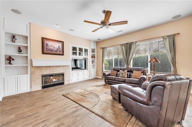 living room featuring a tile fireplace, hardwood / wood-style floors, ceiling fan, and built in shelves