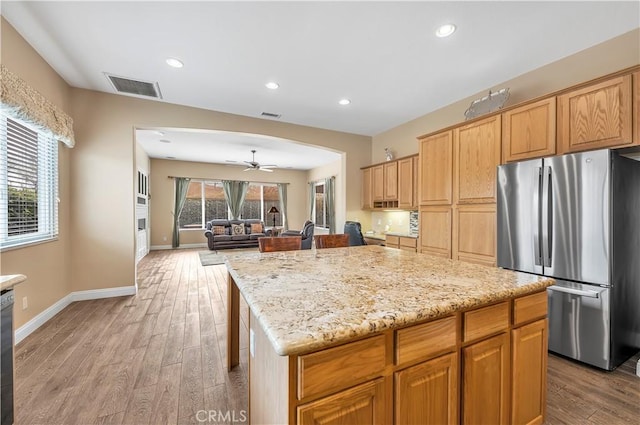 kitchen featuring light stone counters, a center island, stainless steel refrigerator, ceiling fan, and light hardwood / wood-style floors