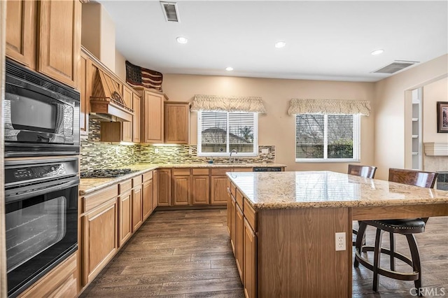 kitchen featuring a center island, black microwave, dark hardwood / wood-style flooring, a kitchen breakfast bar, and light stone countertops