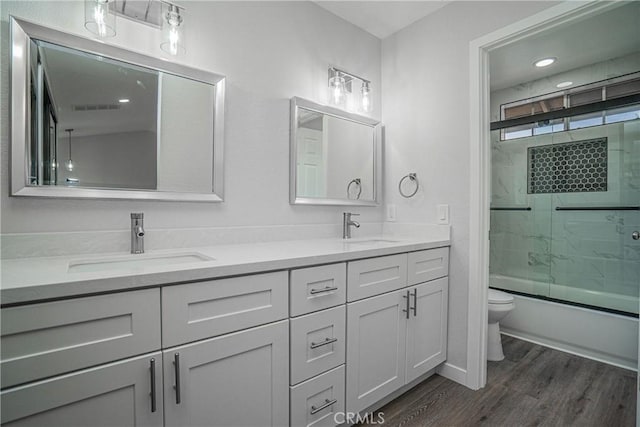 full bathroom with hardwood / wood-style flooring, enclosed tub / shower combo, vanity, and toilet