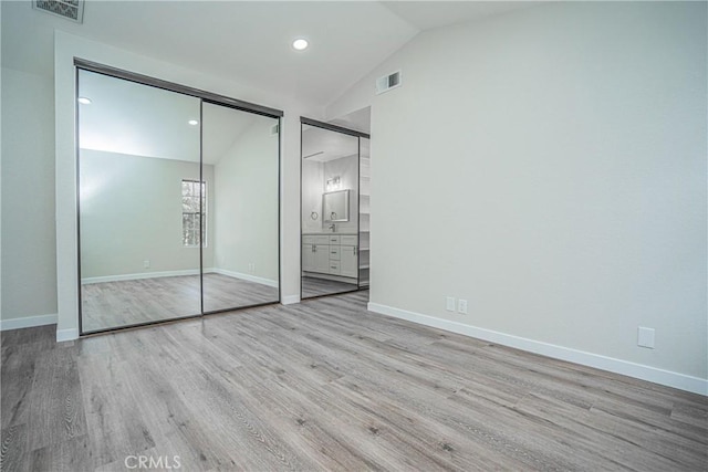 unfurnished bedroom featuring ensuite bath, vaulted ceiling, and light hardwood / wood-style flooring