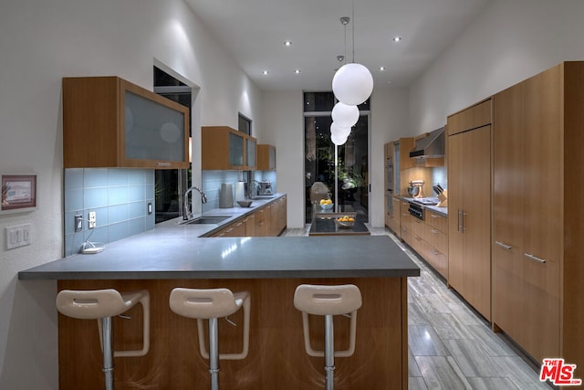 kitchen featuring a breakfast bar, decorative light fixtures, sink, kitchen peninsula, and wall chimney exhaust hood