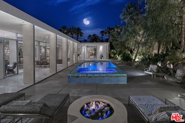 pool at night with an outdoor fire pit, a patio area, and an in ground hot tub