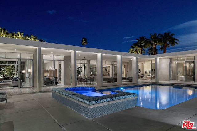 pool at twilight with an in ground hot tub and a patio