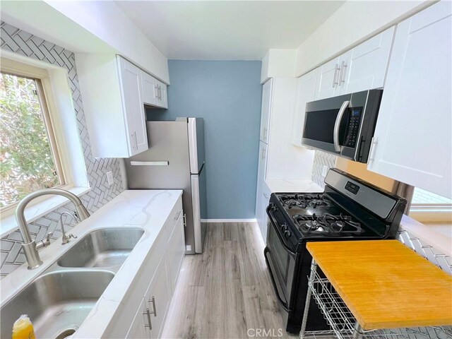 kitchen featuring appliances with stainless steel finishes, sink, white cabinets, backsplash, and light hardwood / wood-style floors