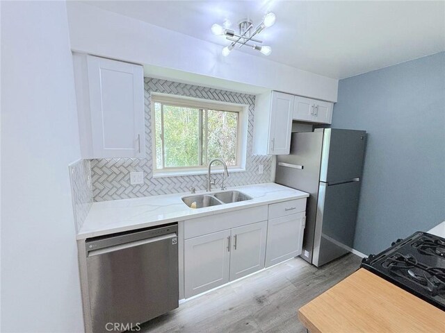 kitchen featuring sink, appliances with stainless steel finishes, white cabinetry, light hardwood / wood-style floors, and decorative backsplash