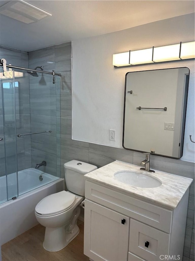 full bathroom featuring hardwood / wood-style flooring, enclosed tub / shower combo, tile walls, vanity, and toilet