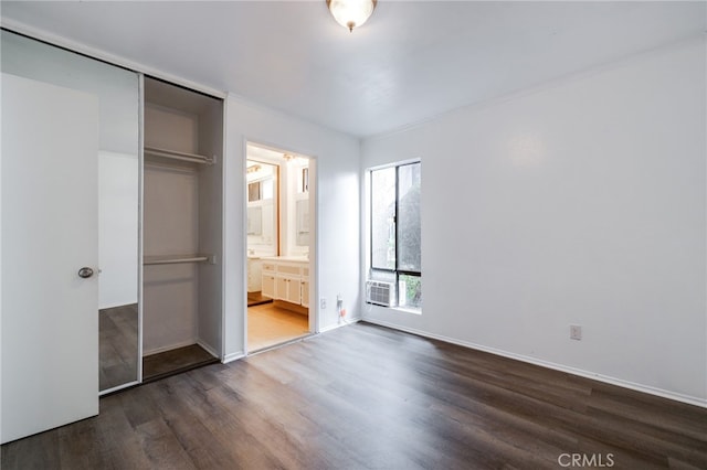 unfurnished bedroom with ensuite bath, cooling unit, dark wood-style floors, and baseboards