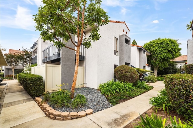 view of side of property featuring stucco siding, a tile roof, and fence