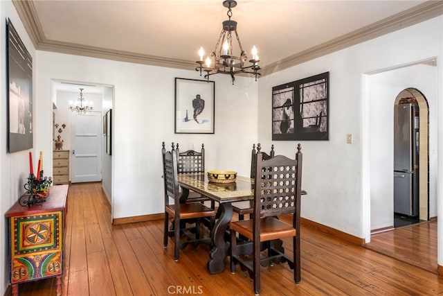 dining space with hardwood / wood-style flooring, crown molding, and an inviting chandelier