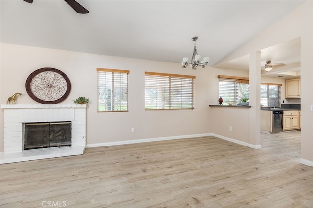 unfurnished living room featuring light wood-type flooring, ceiling fan with notable chandelier, a brick fireplace, and a healthy amount of sunlight