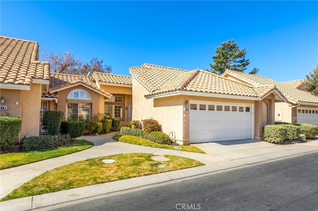 mediterranean / spanish-style home featuring stucco siding, an attached garage, a tile roof, and concrete driveway