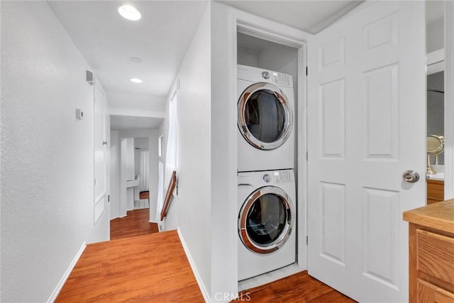 washroom featuring stacked washer and clothes dryer, baseboards, recessed lighting, wood finished floors, and laundry area