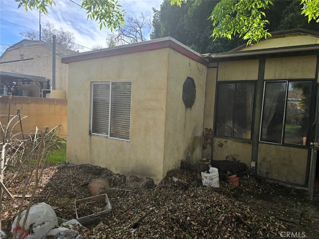 view of side of home with stucco siding and fence