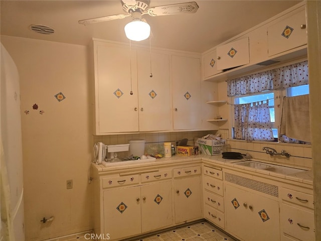 kitchen with tasteful backsplash, tile counters, light floors, white cabinets, and a sink