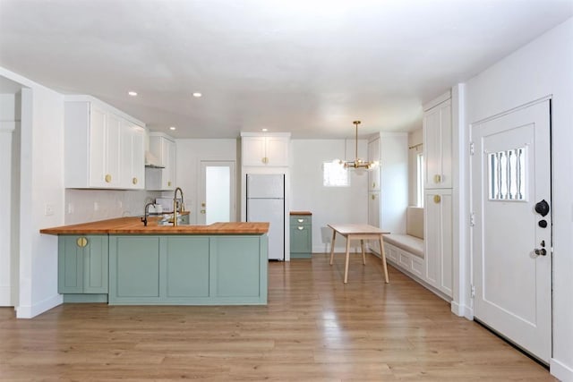 kitchen featuring wood counters, decorative light fixtures, white cabinetry, white refrigerator, and kitchen peninsula