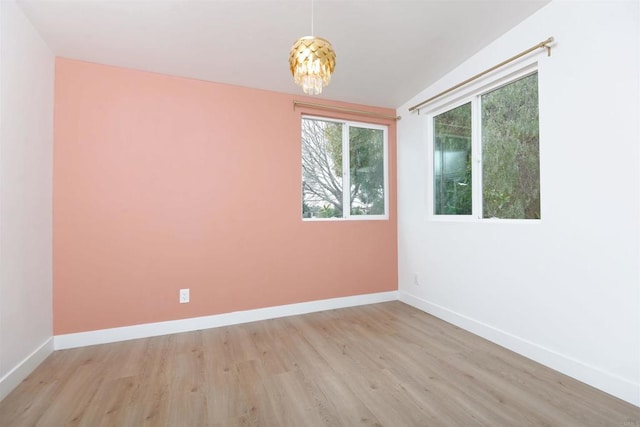 empty room with a chandelier, light wood finished floors, and baseboards