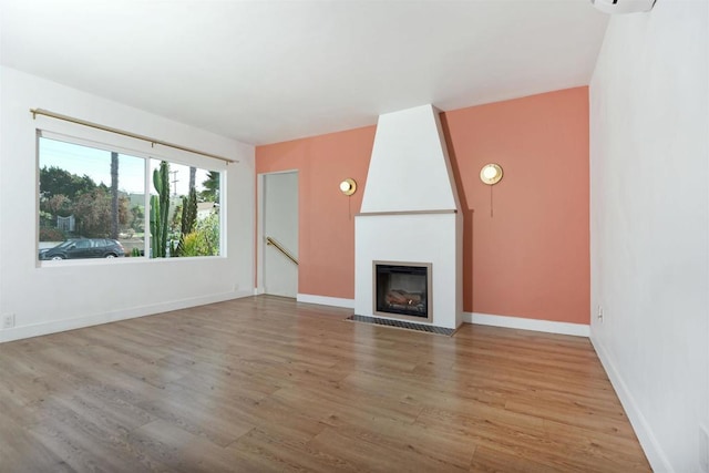 unfurnished living room with a large fireplace, baseboards, and wood finished floors