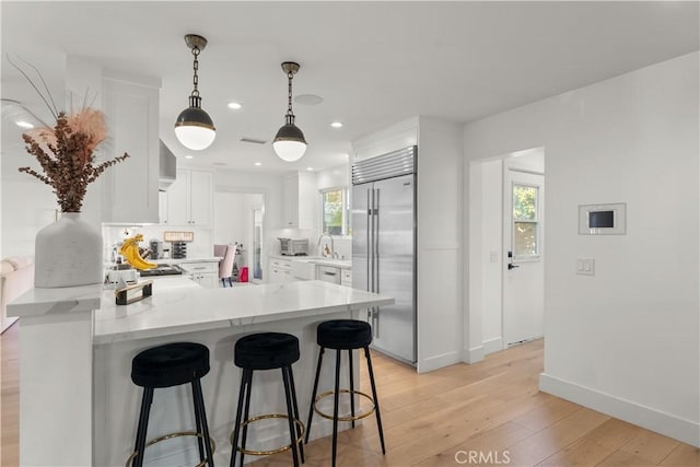 kitchen with built in fridge, white cabinetry, hanging light fixtures, light hardwood / wood-style floors, and kitchen peninsula