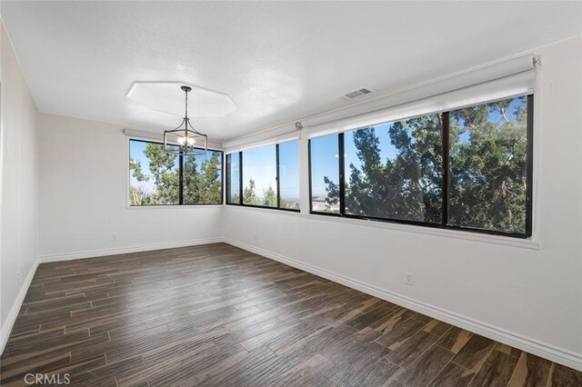 spare room featuring dark wood-type flooring and a chandelier