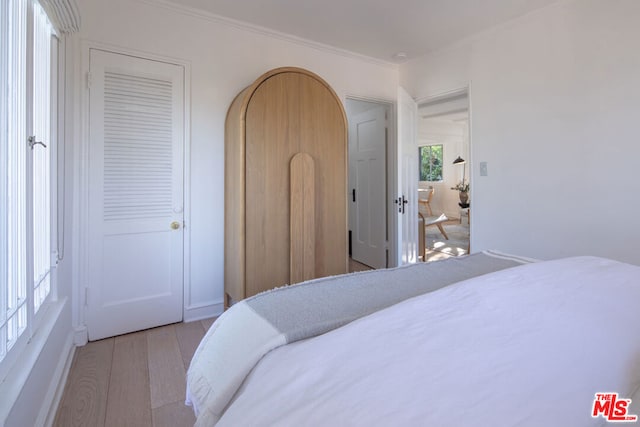 bedroom with crown molding, multiple windows, and light hardwood / wood-style flooring