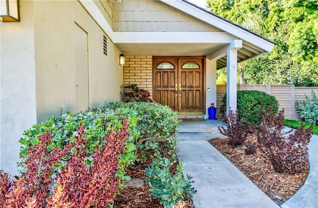 view of exterior entry with brick siding, fence, and stucco siding