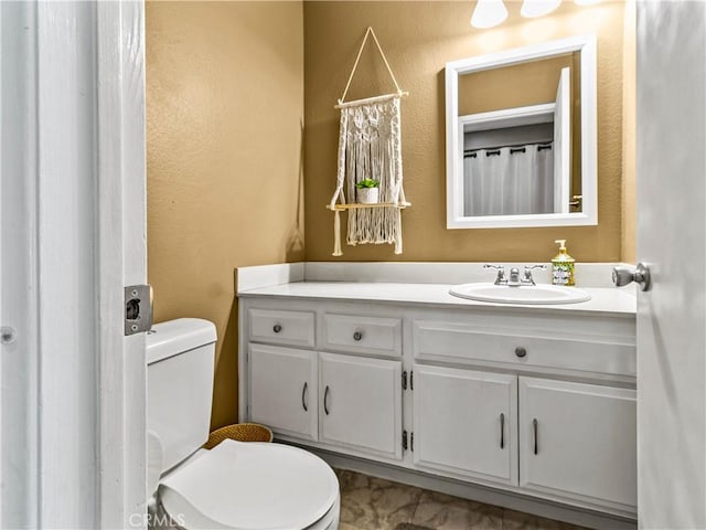 bathroom featuring vanity, toilet, and a textured wall