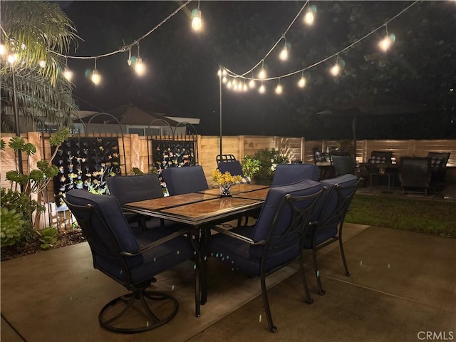 patio at night featuring outdoor dining area and fence