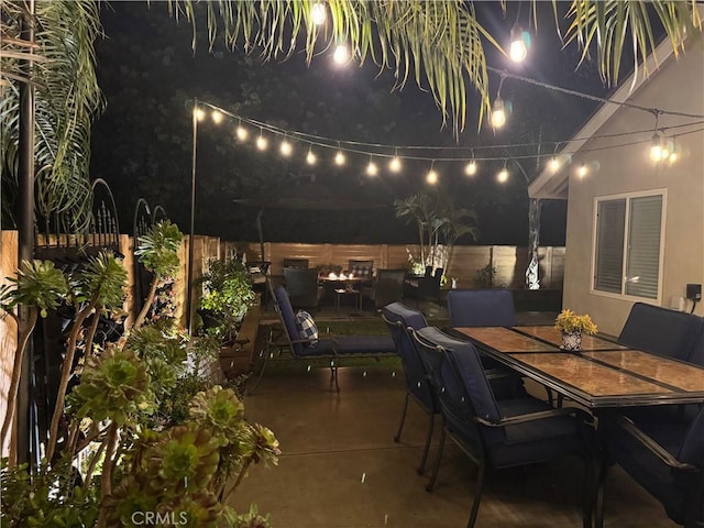 patio at night featuring outdoor dining area and a fenced backyard