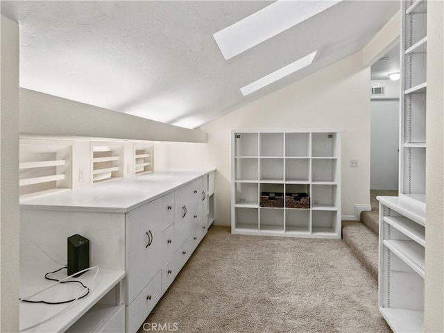 interior space with visible vents, vaulted ceiling with skylight, and light carpet