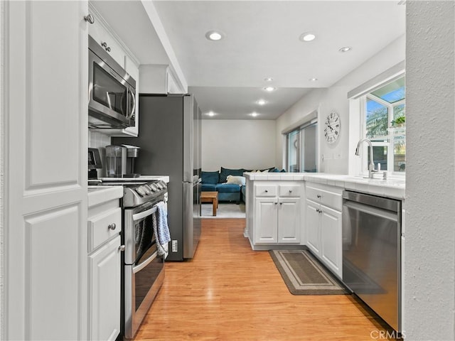 kitchen with tile counters, open floor plan, light wood-type flooring, appliances with stainless steel finishes, and white cabinetry