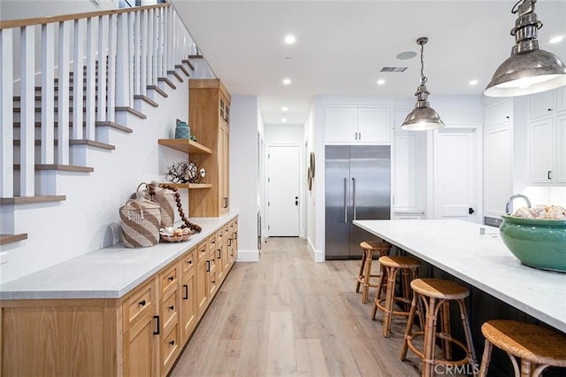 kitchen with decorative light fixtures, white cabinets, a kitchen breakfast bar, built in refrigerator, and light stone countertops