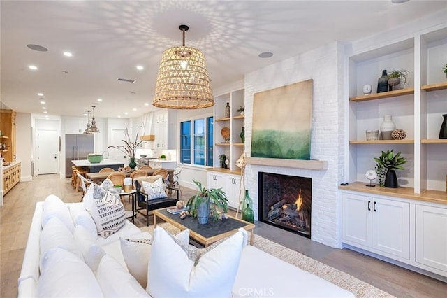 living room featuring a brick fireplace, built in shelves, light hardwood / wood-style flooring, and a notable chandelier