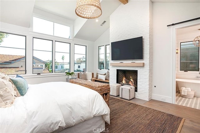 bedroom featuring a barn door, ensuite bath, high vaulted ceiling, a fireplace, and hardwood / wood-style floors